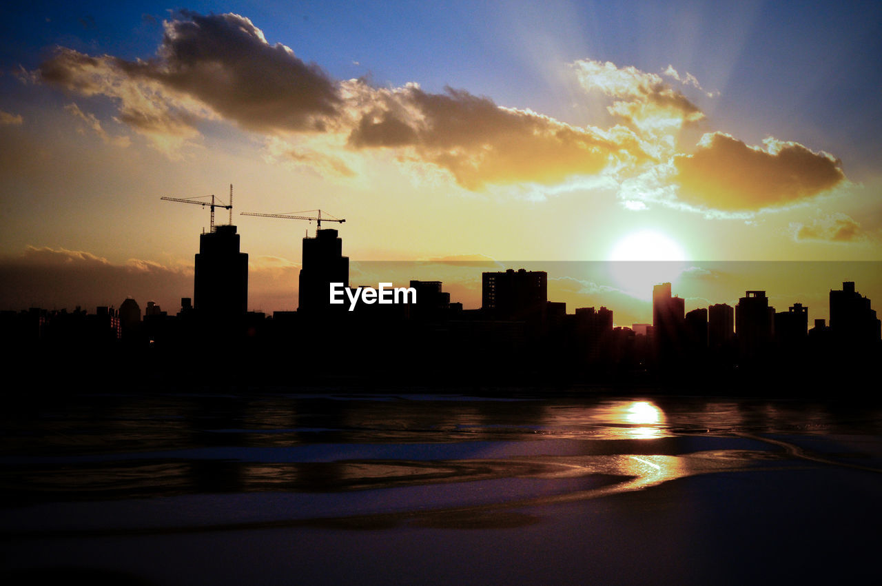 Silhouette city by sea against sky during sunset