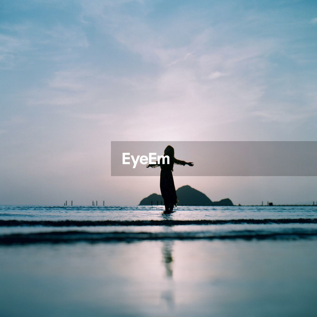 Mid distance view of woman with arms outstretched standing in sea against sky