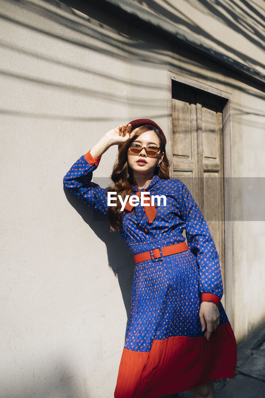 Portrait of young woman wearing sunglasses against wall outdoors