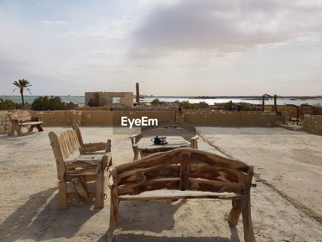 Empty chairs and table at beach against sky