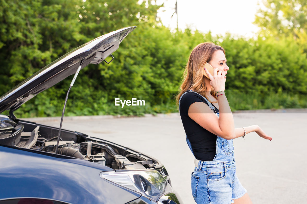 MIDSECTION OF WOMAN STANDING ON CAR AGAINST SKY