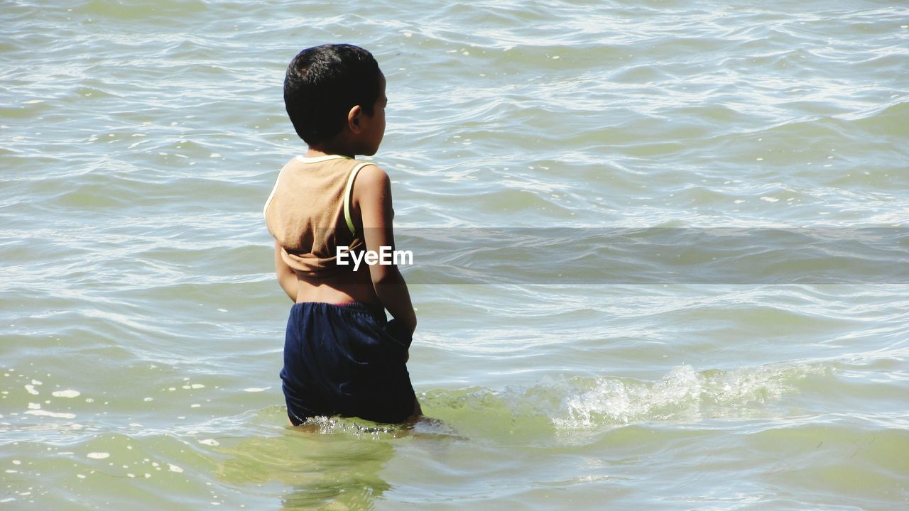 REAR VIEW OF SHIRTLESS BOY STANDING ON SEA