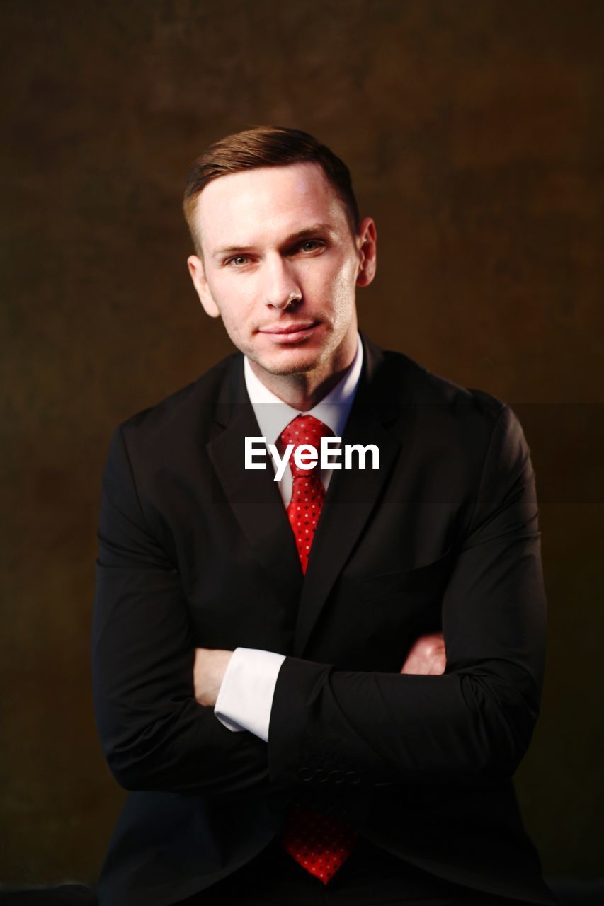 Portrait of mid adult businessman with arms crossed against colored background