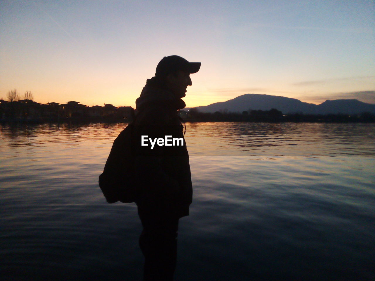 Silhouette man standing by lake against sky during sunset