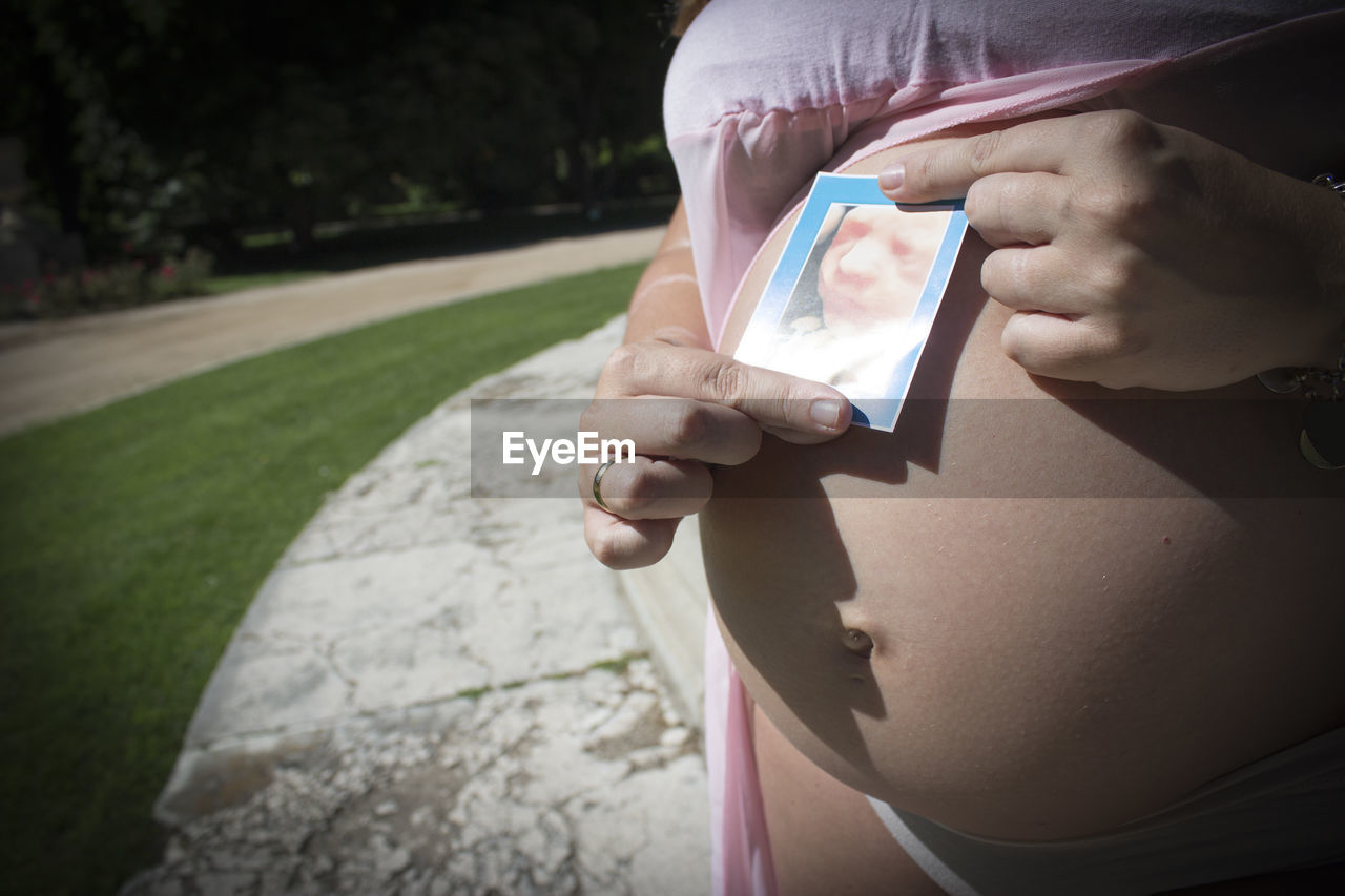 Seven month pregnant woman with ultrasound of baby on her gut. pink dress color