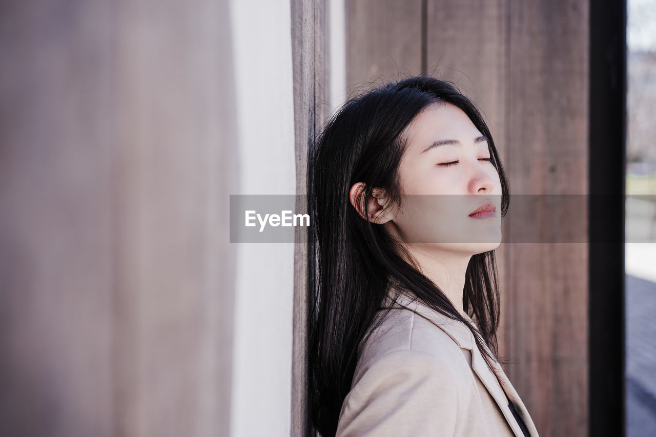 Relaxed beautiful chinese business woman standing over wood signs background with eyes closed