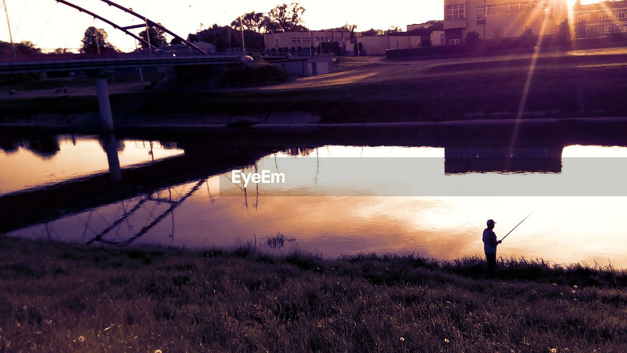 SILHOUETTE MAN STANDING ON RIVERBANK AGAINST SKY