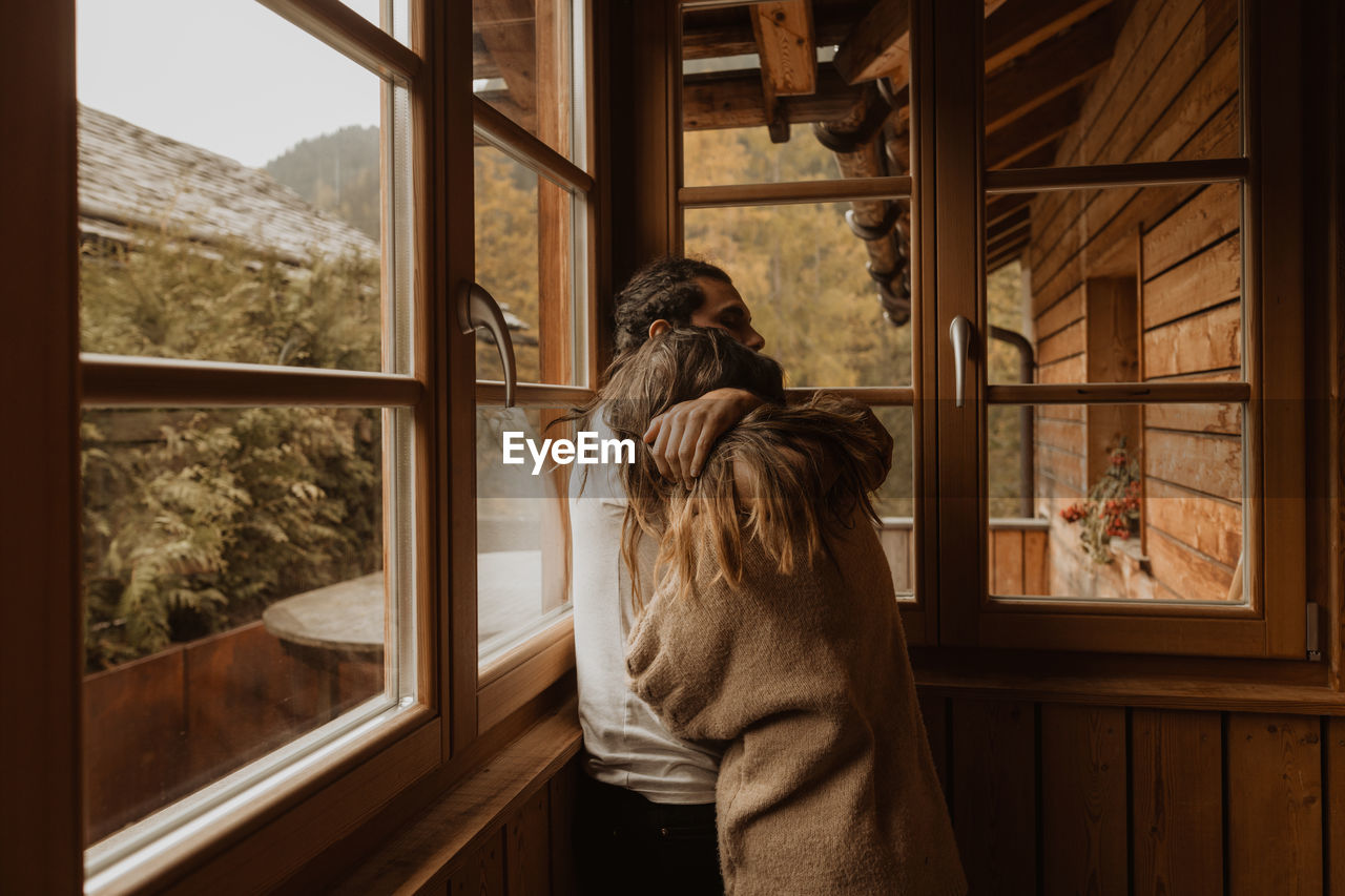 Side view of man embracing anonymous girlfriend while spending time together in wooden cabin in daylight