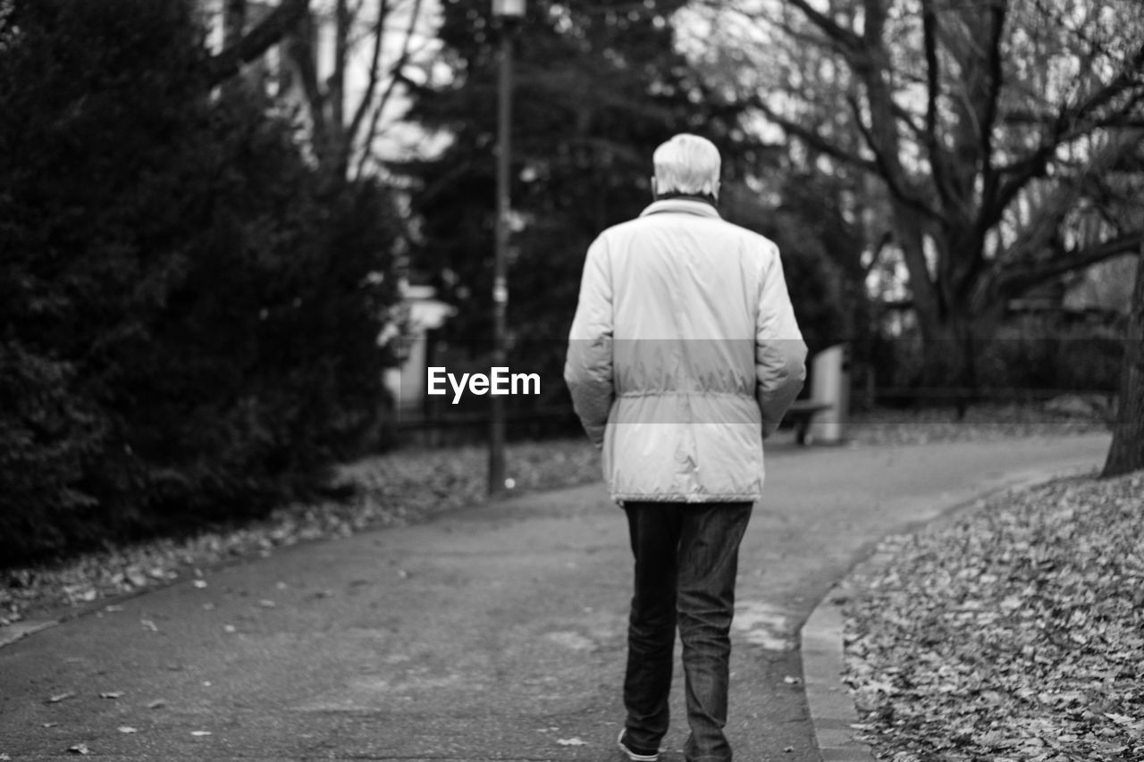 REAR VIEW OF MAN WITH UMBRELLA WALKING ON ROAD