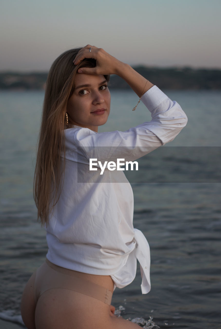 Beautiful woman sitting at beach against sky