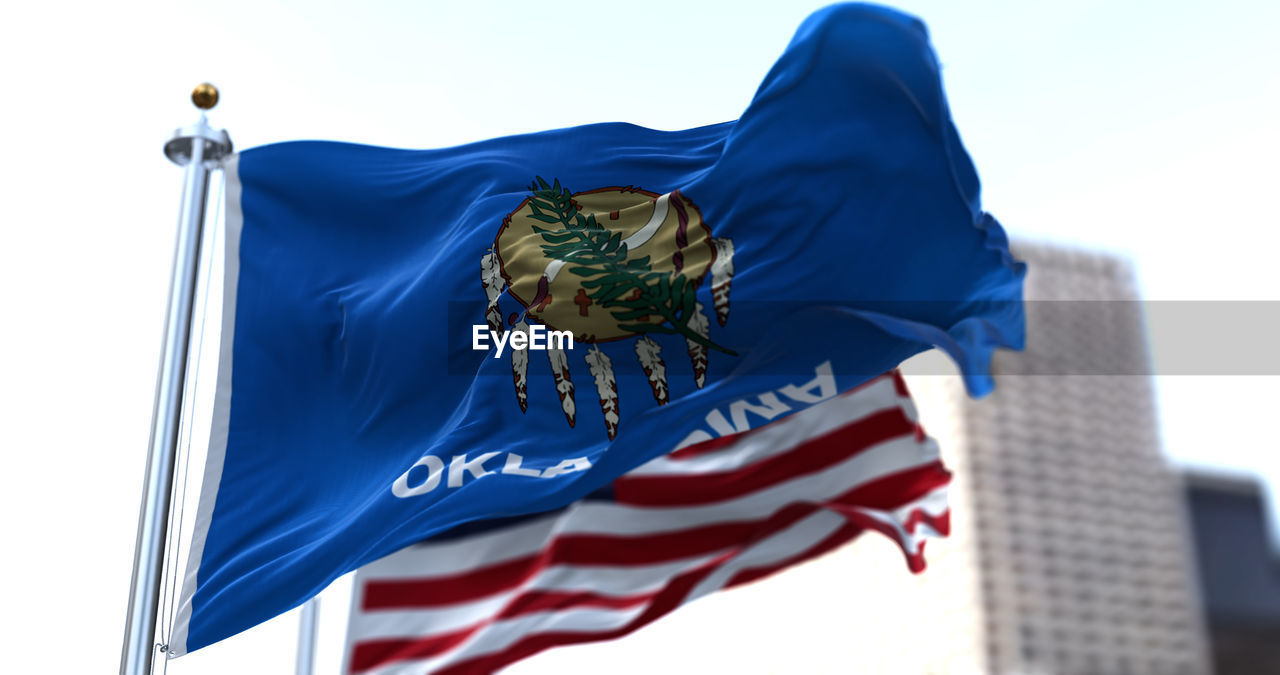 The flags of the oklahoma state and united states of america waving in the wind. 