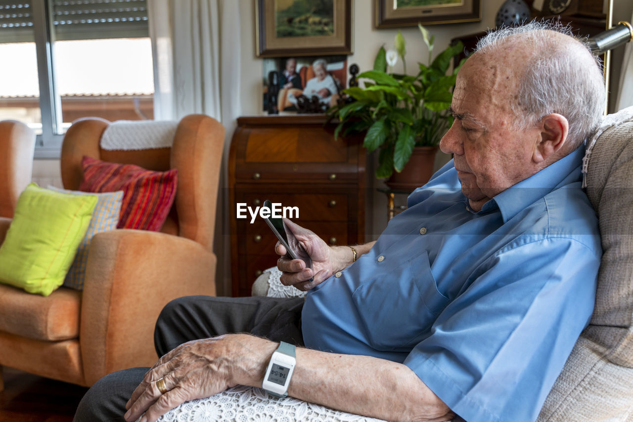 Elderly man using a mobile phone and wearing a smart emergency alarm bracelet around wrist at home