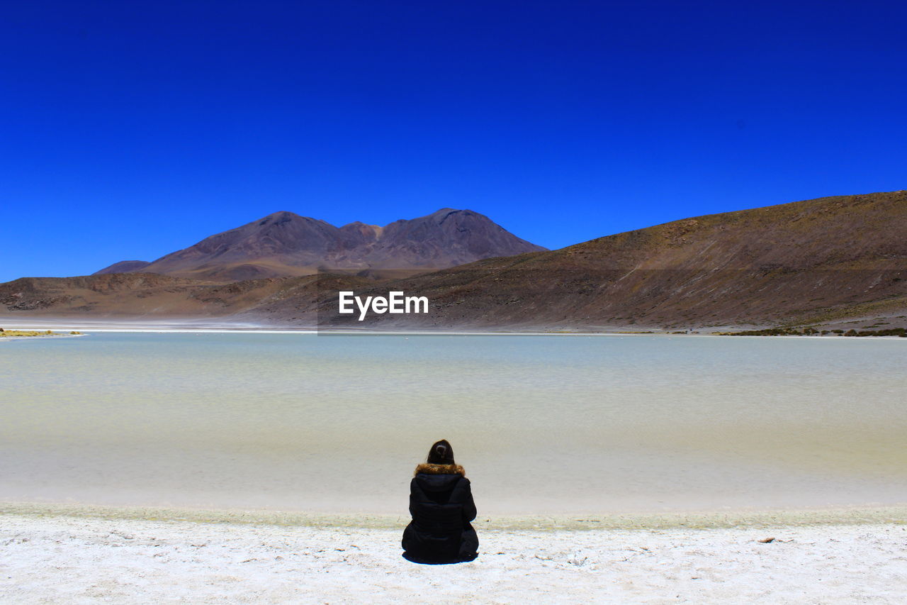 REAR VIEW OF WOMAN ON SHORE AGAINST SKY