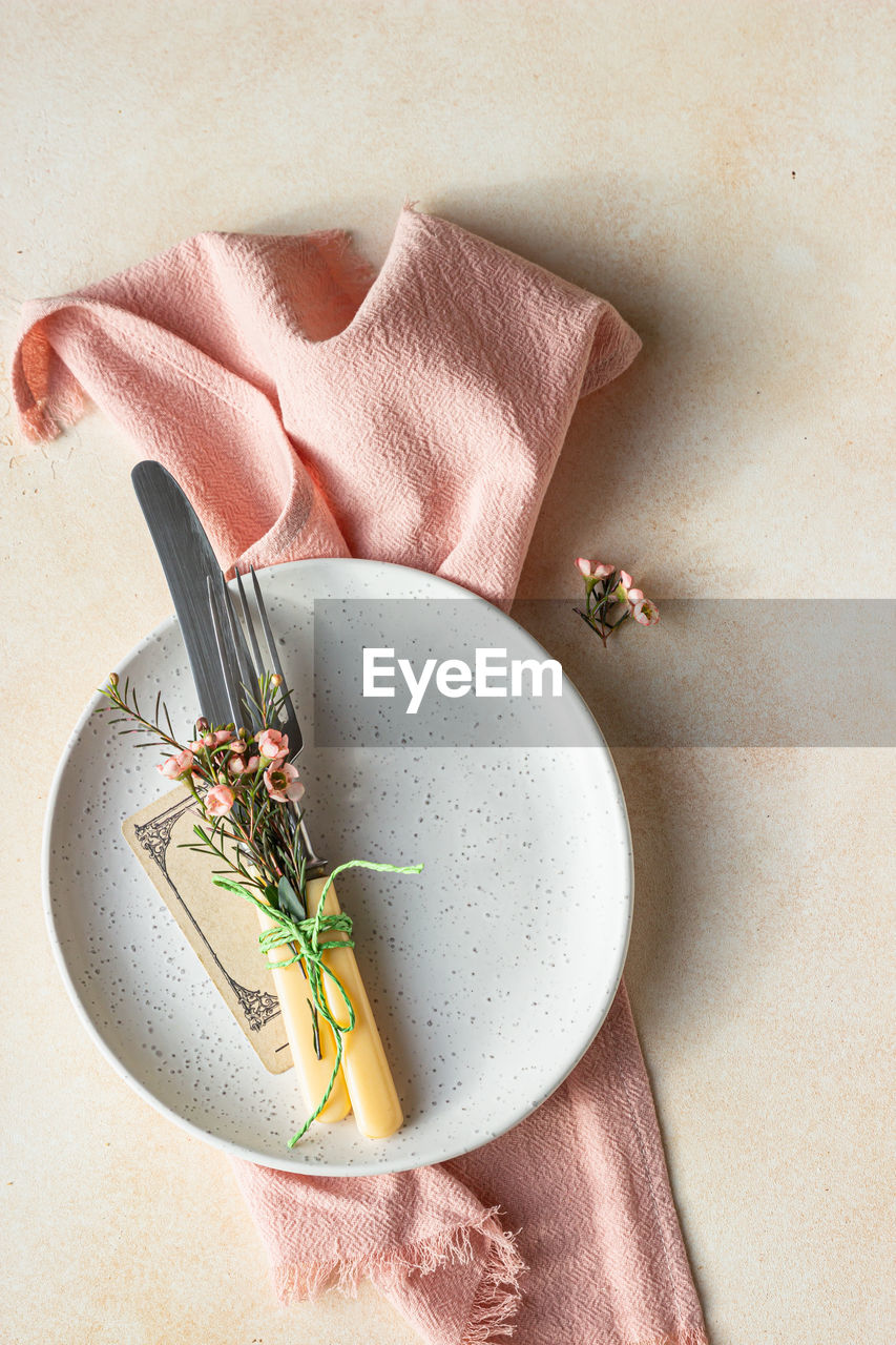 Romantic or spring table setting. knife and fork, little pink flowers and linen napkin on a plate.