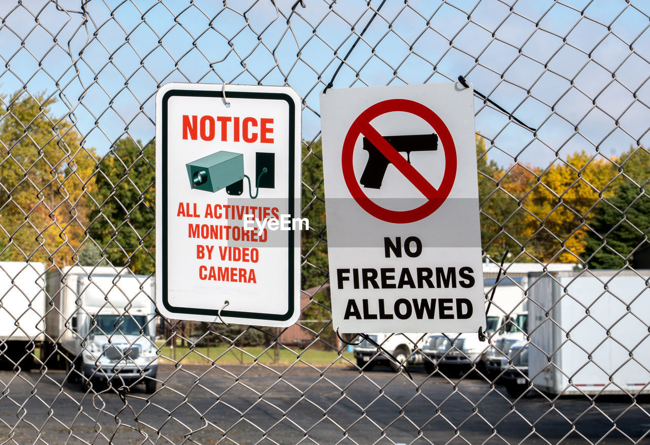 Signs on a chain link fence  says no firearms are allowed and video cameras are monitoring the area.