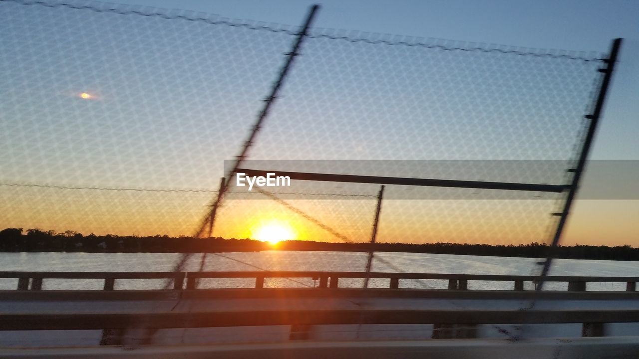 Bridge by chainlink fence against sky during sunset