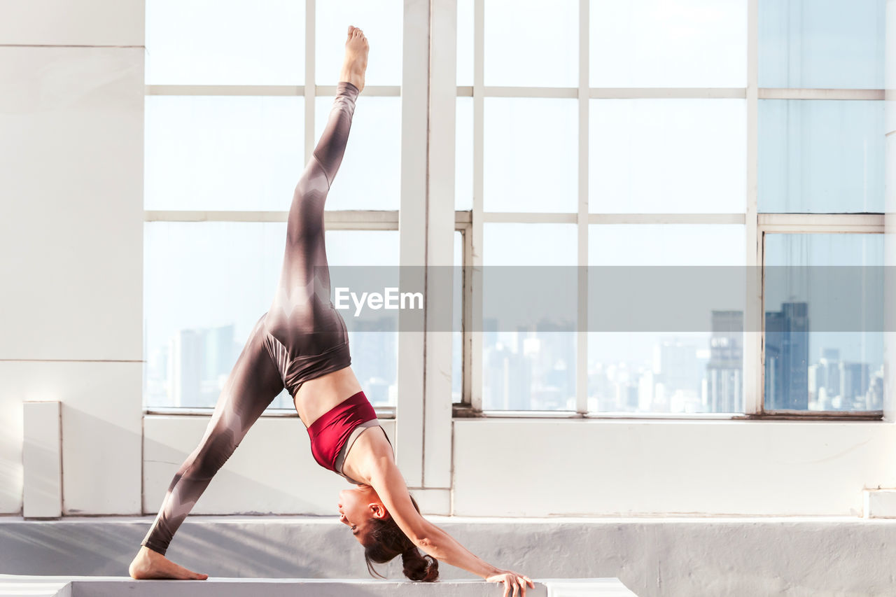 Full length side view of young woman practicing yoga at home