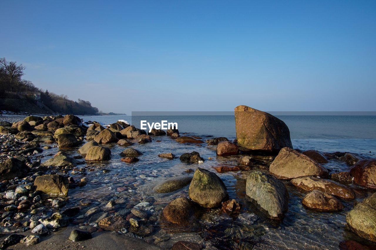 Scenic view of sea and rocks against clear sky