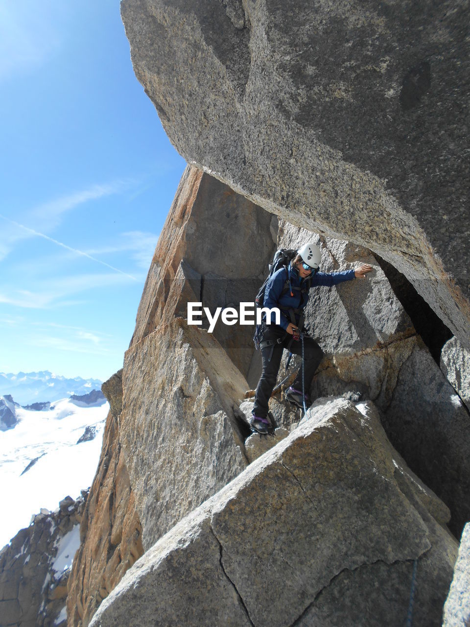 Low angle view of climber on rock by snowcapped mountain against sky