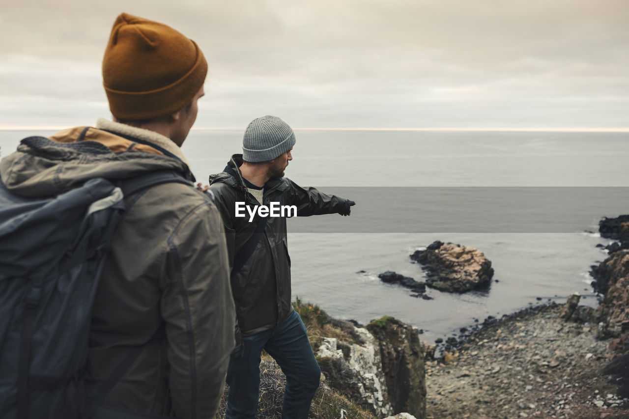 Man pointing at rock in sea to male friend during vacation