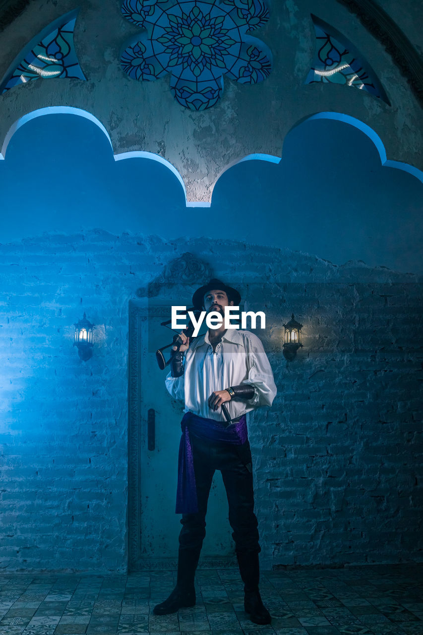 Portrait of man in costume standing against door of abandoned building at night