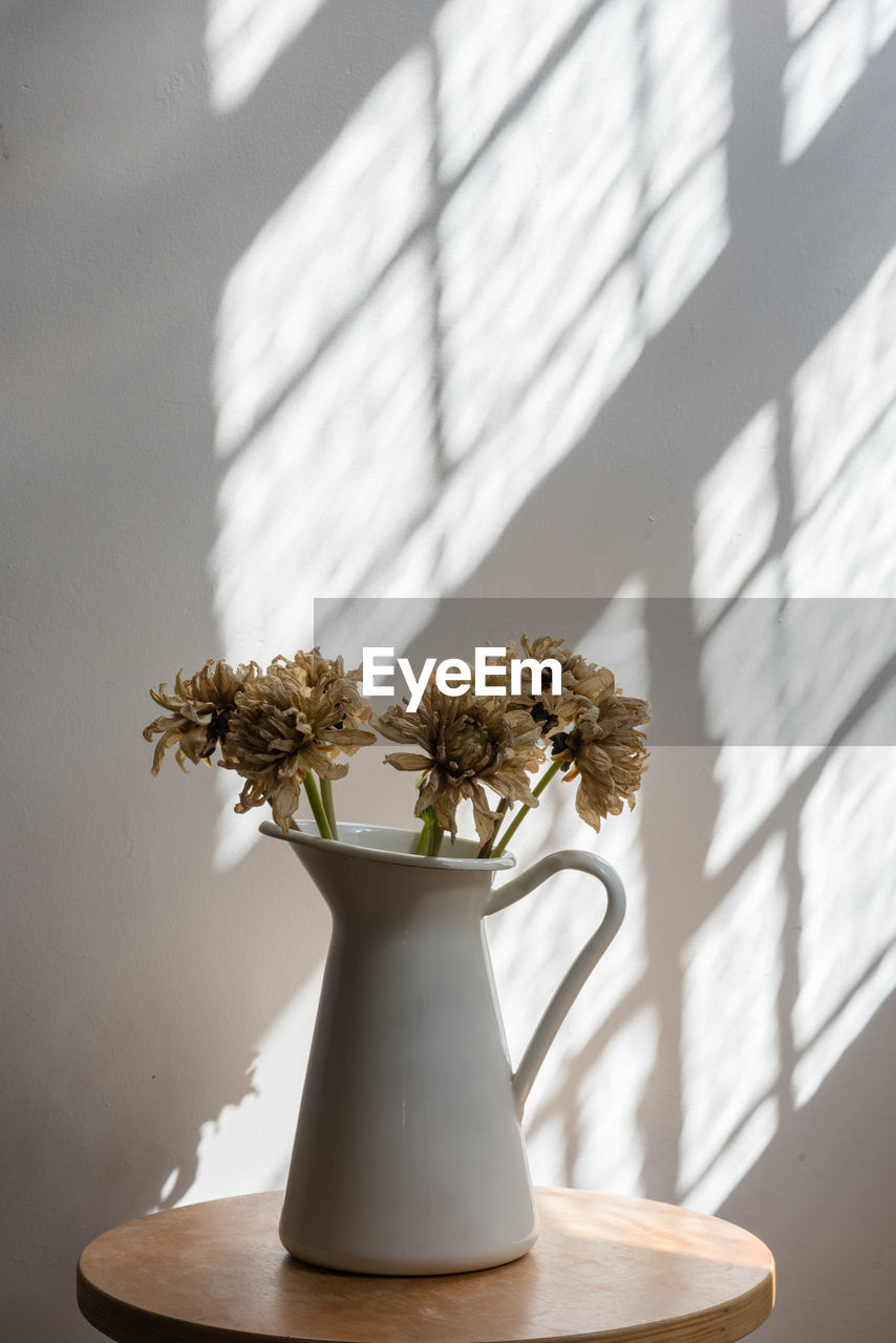 Close-up of flowers in vase on wooden table against wall