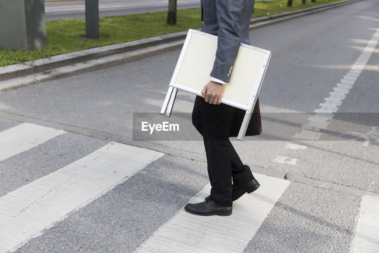 Low section of real estate agent carrying placard while crossing street