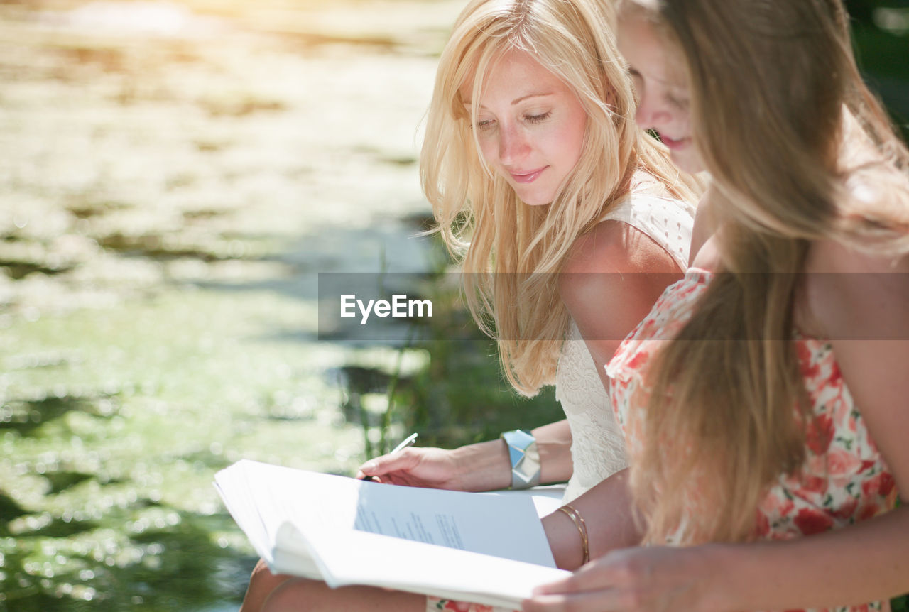 Smiling woman looking at friend writing in book at park