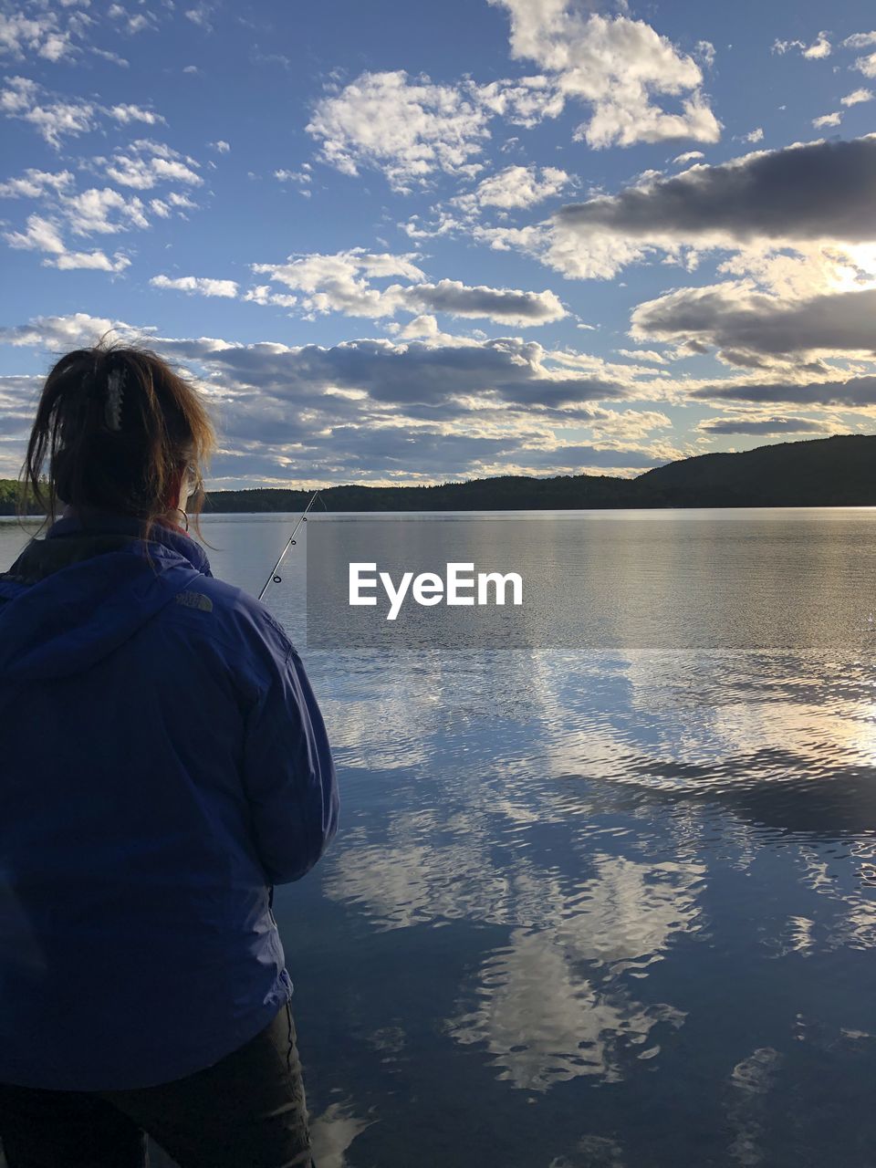 REAR VIEW OF WOMAN STANDING BY LAKE AGAINST SKY DURING SUNSET