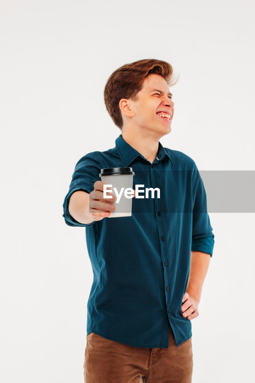 Cheerful young man holding coffee cup against white background