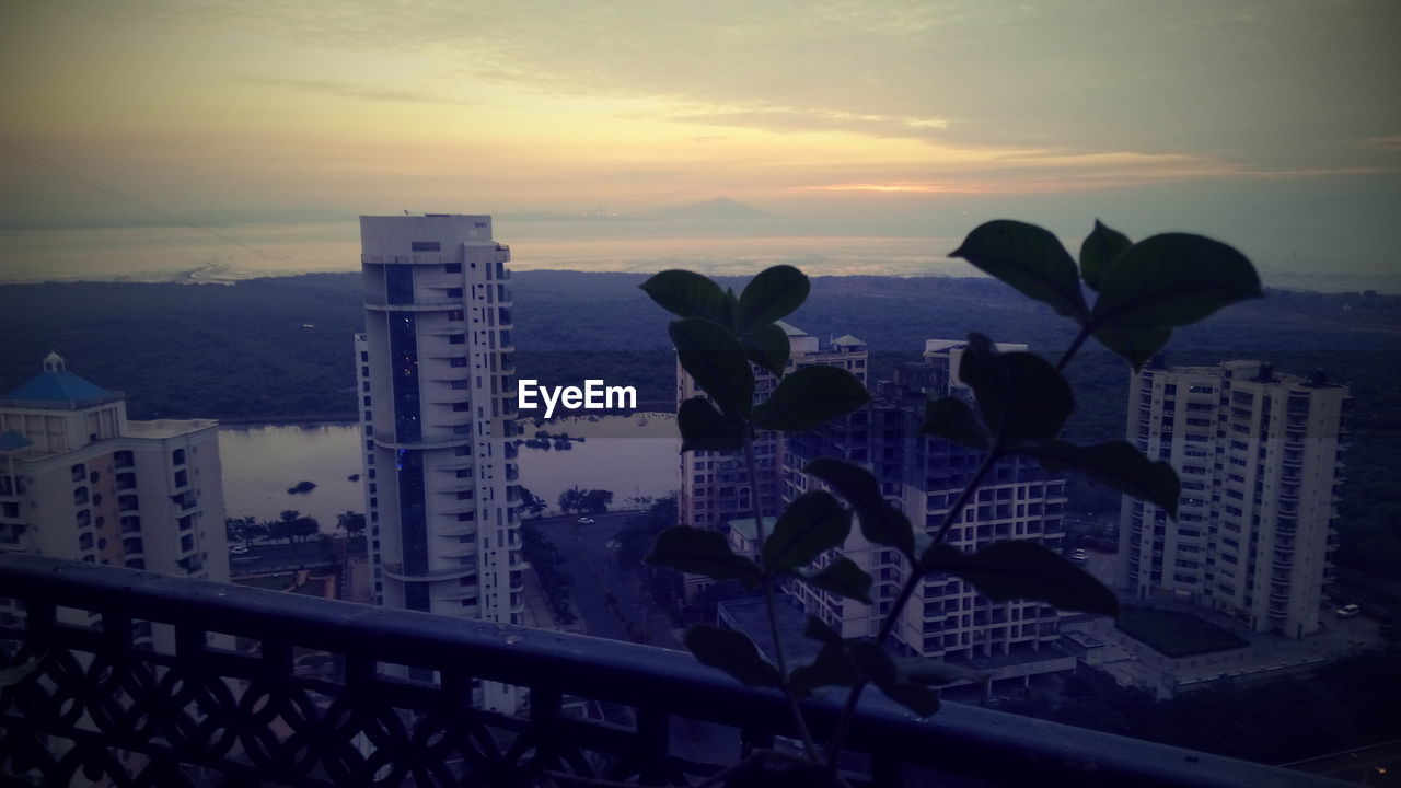 Cityscape by sea against sky during sunset