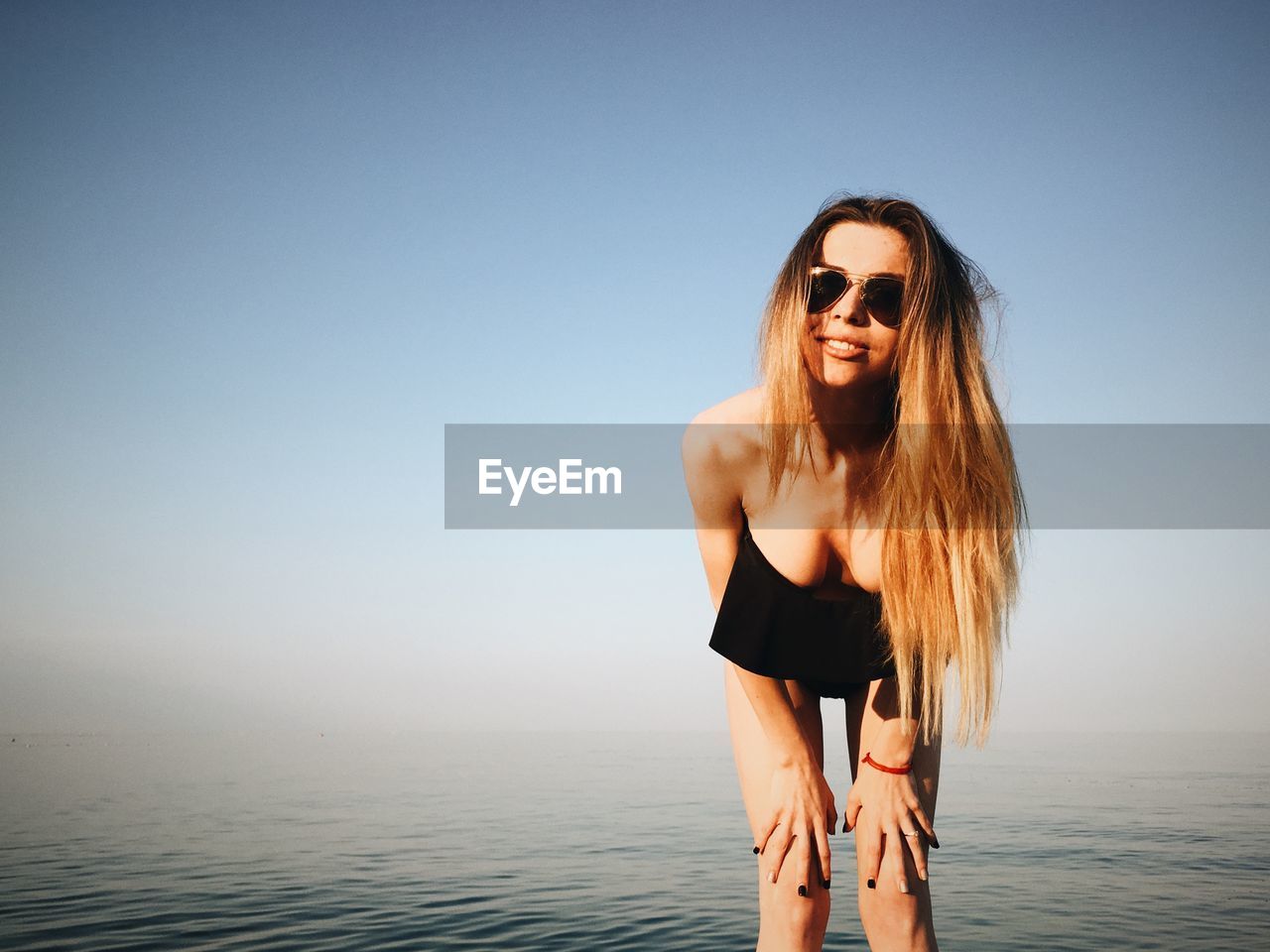 Portrait of beautiful woman wearing sunglasses at beach against clear blue sky