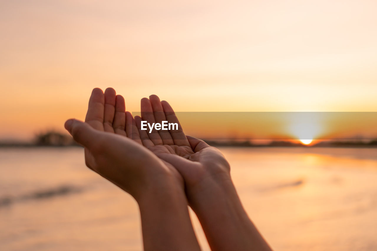 Midsection of person relaxing against orange sky during sunset