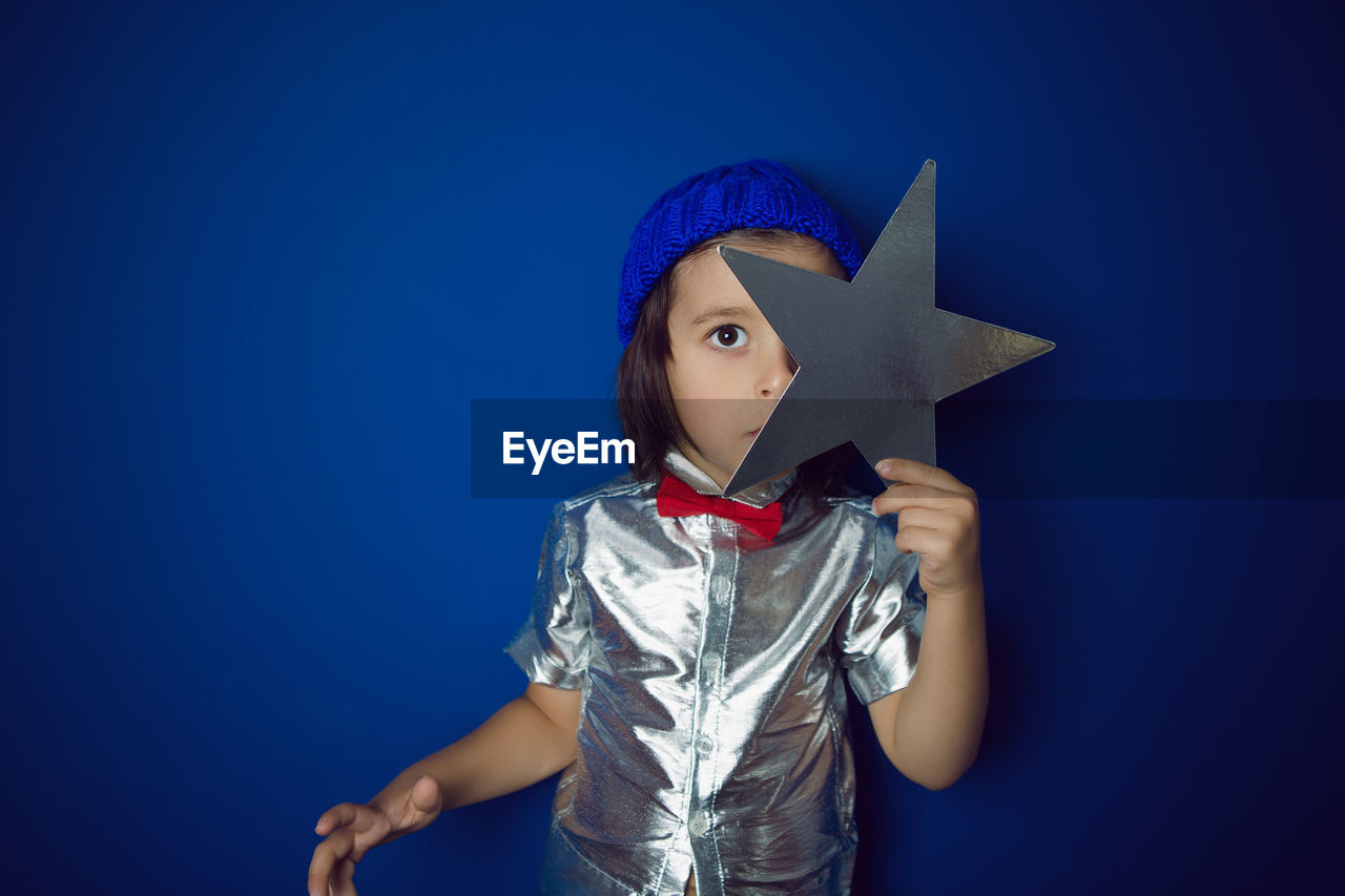 Christmas boy child holding a star in a silver shirt blue hat and red bow tie stands in the studio