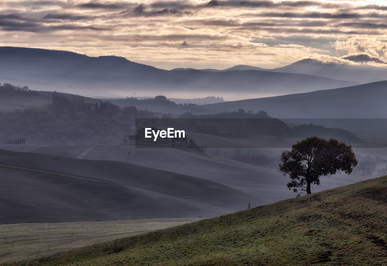 Scenic view val d'orcia landscape against sky during sunset