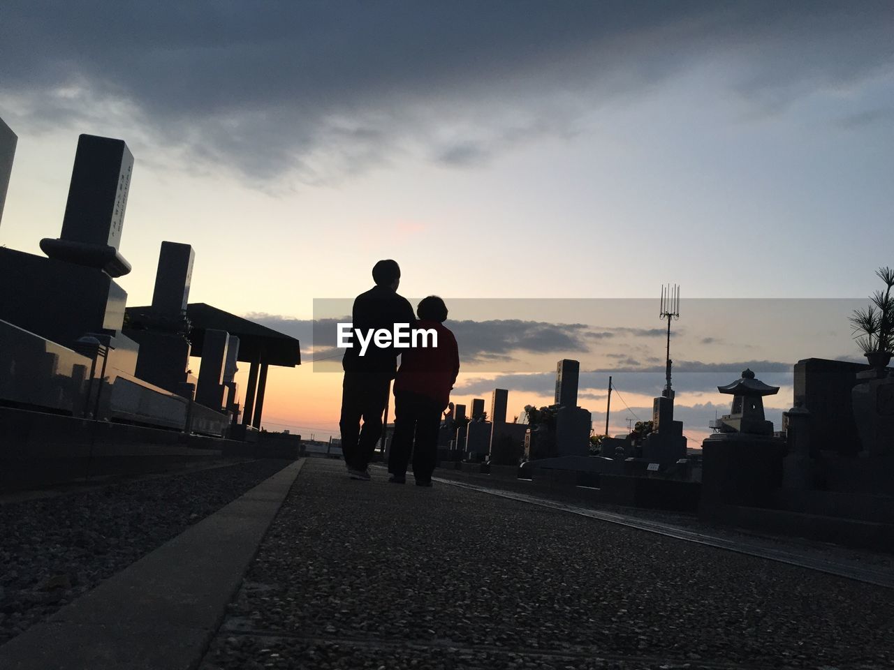 Rear view of people walking on footpath against sky during sunset