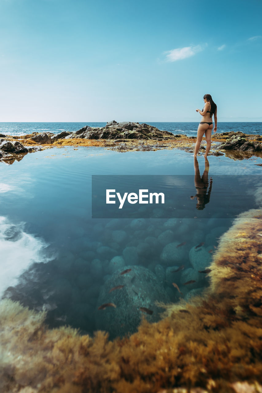 Reflection of woman on sea against sky