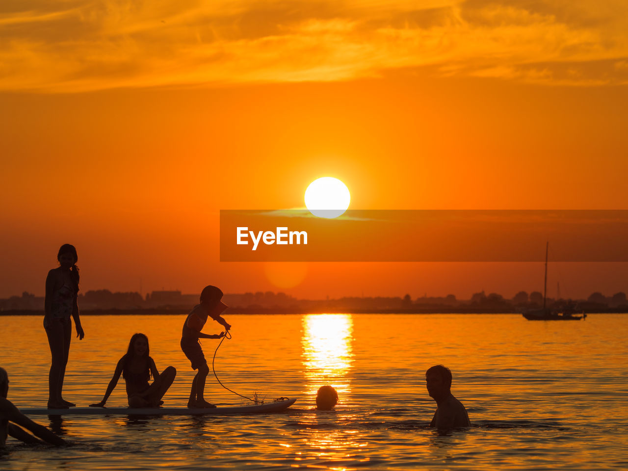 Silhouette people paddleboarding on sea against orange sky during sunset