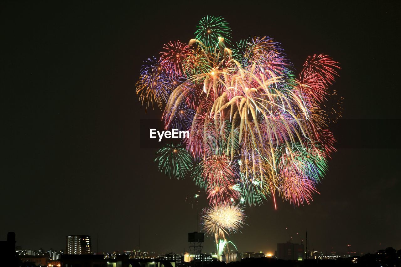 Low angle view of colorful firework exploding over illuminated city