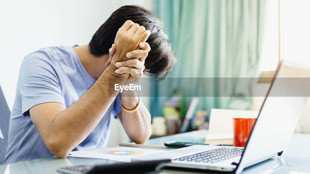 REAR VIEW OF MAN USING LAPTOP