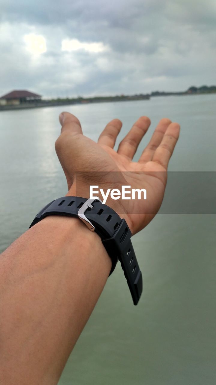 Cropped hand of man wearing wristwatch against sea 