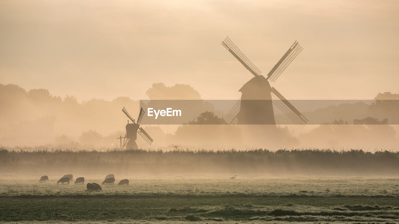 Traditional windmill on field against sky during sunrise