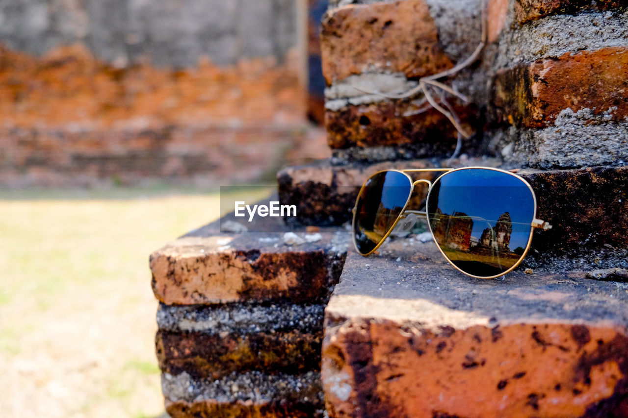 CLOSE-UP OF SUNGLASSES ON RETAINING WALL AGAINST STONE