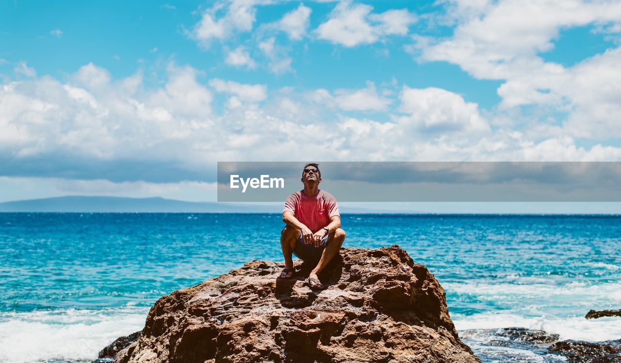 Man sitting on rock against blue sea