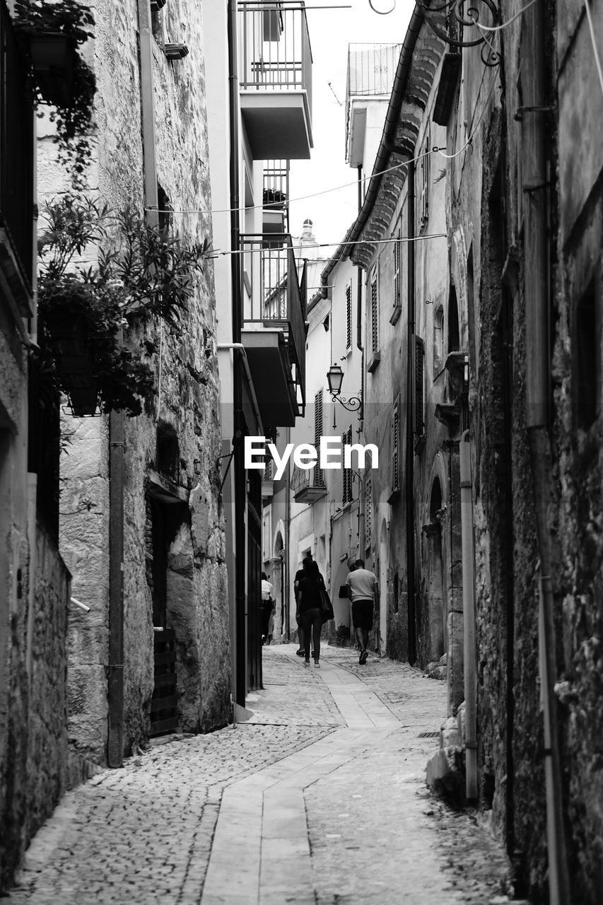 PEOPLE WALKING ON NARROW ALLEY AMIDST BUILDINGS