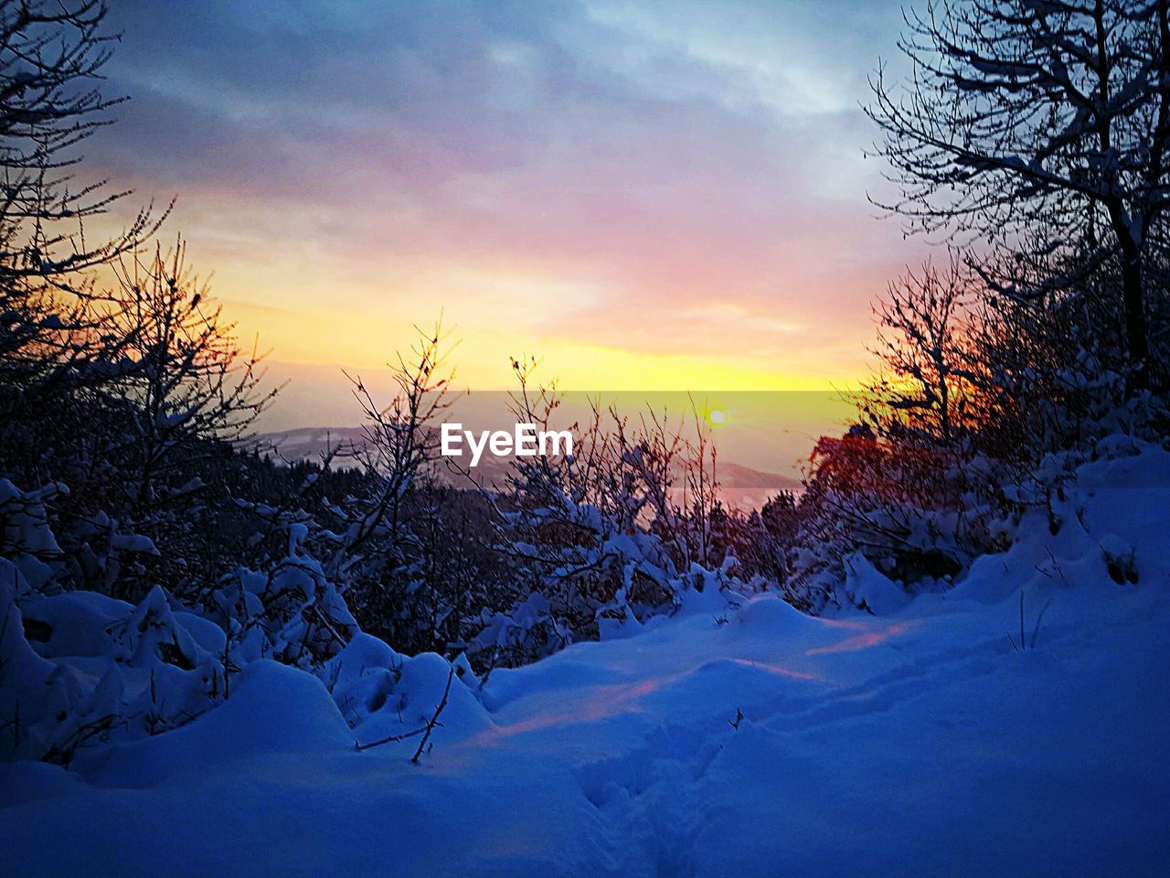 SNOW COVERED LANDSCAPE AGAINST SKY DURING SUNSET