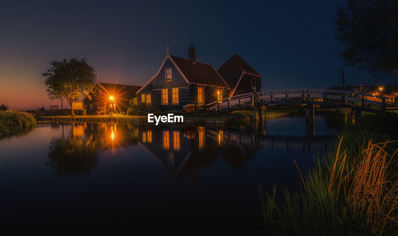 ILLUMINATED BUILDINGS BY LAKE AT NIGHT