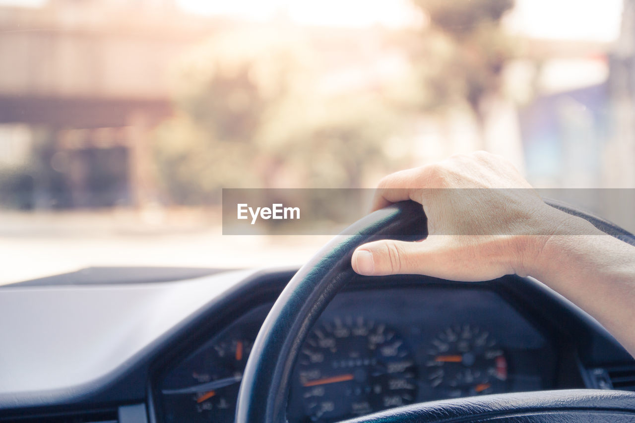 A man drives a car holding steering wheel by one hand in the evening