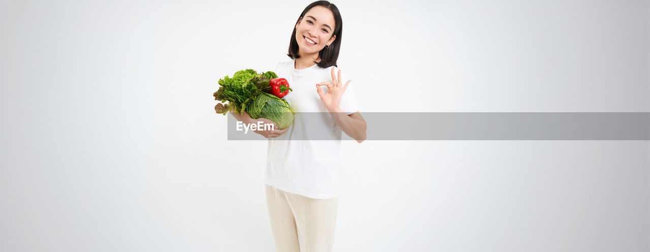 studio shot, women, indoors, adult, one person, clothing, flower, freshness, flowering plant, food, plant, wellbeing, dress, food and drink, bouquet, young adult, holding, bride, photo shoot, wedding dress, person, healthy eating, smiling, emotion, flower arrangement, happiness, copy space, standing, vegetable, rose, white, portrait, female, hand, nature, gown, positive emotion, lifestyles, white background, human face, fashion, long hair, hairstyle, spring, celebration