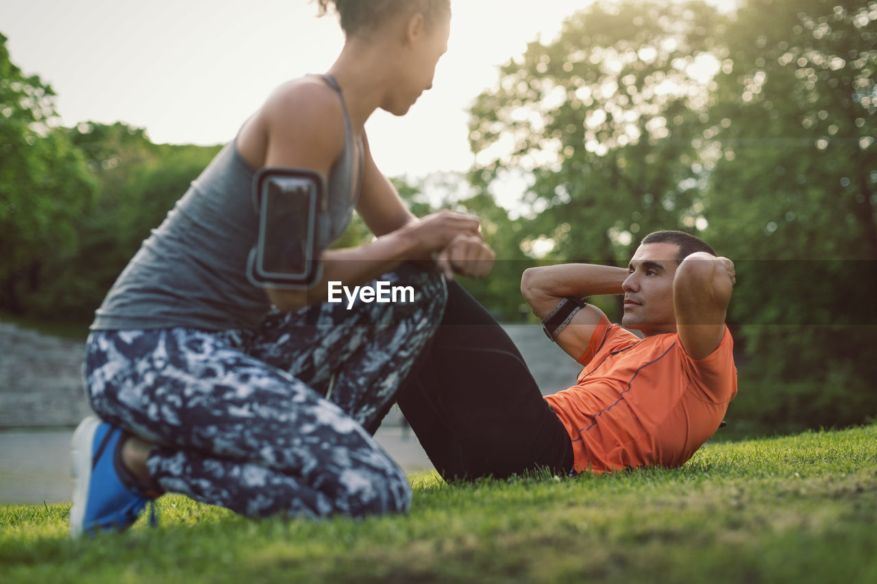 Woman kneeling and looking at man doing sit-ups at park